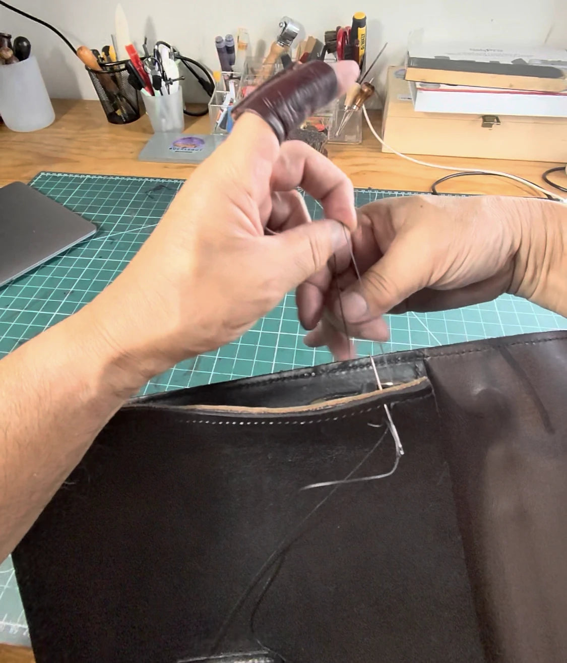 A craftsman hand stitching a leather bag at the workbench
